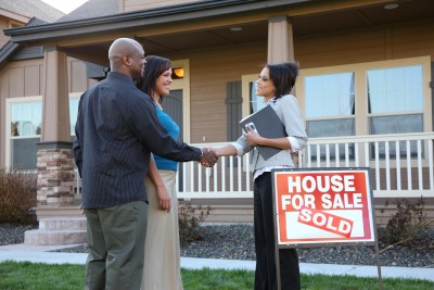 Couple shaking hands with realtor in front of their new house.