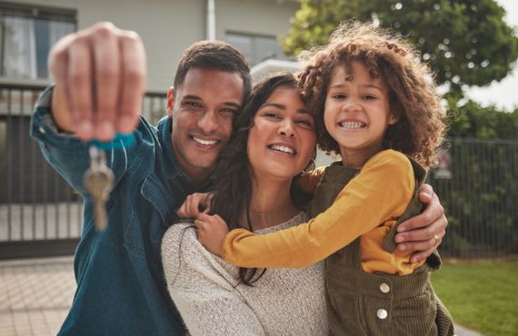Family in front of new house holding key and smiling.