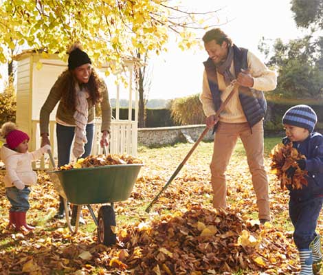 two small children help parents rake leaves in their yard