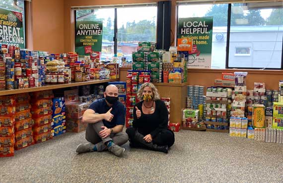 Timberland Bank Loan Officers Mac Pinch and Jannae Mitton pose in front of 5,000 donated food items for Gig Harbor food drive