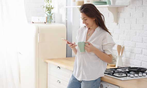 consumer uses smartphone in their kitchen while drinking coffee