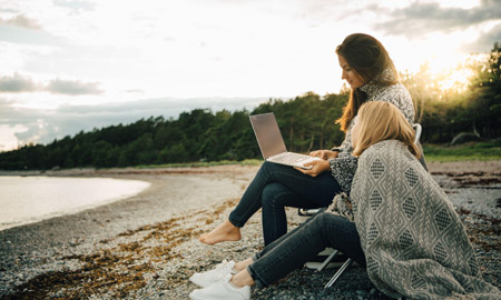 two women on the beach looking at a computer