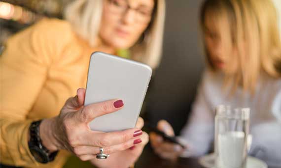 two customers look at smartphones together while drinking water and coffee in a cafe