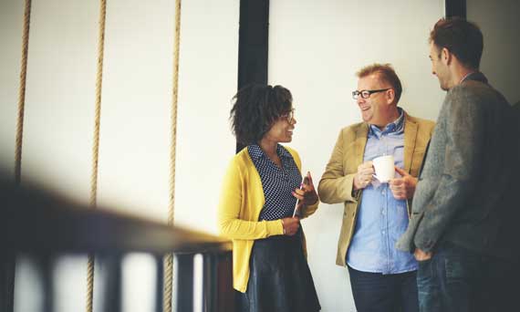 group of three coworkers talk and laugh together on the way to a meeting