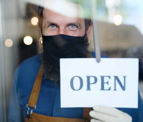 business owner wearing a mask smiles while putting the open sign on their window
