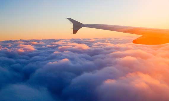 airplane wing flying above the clouds during sunset