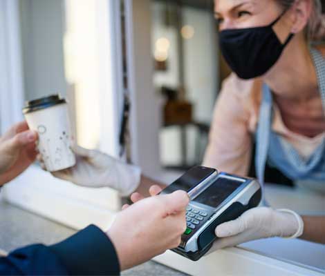 barista wearing a mask hands coffee to customer while they pay using their phone