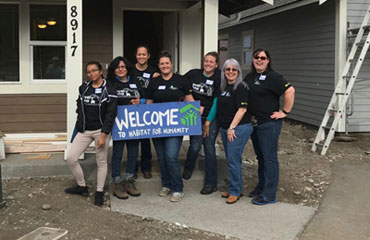 Group holds "Welcome to Habitat for Humanity" sign in front of work site