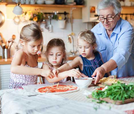 Grandparent helps three grandchildren prepare homemade pizza for a dinner together